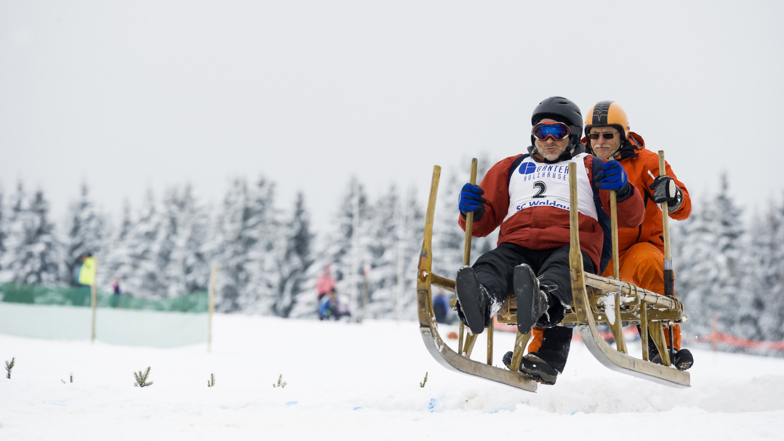 Zwei Personen rasen auf einem Hornschlitten durch den Schnee