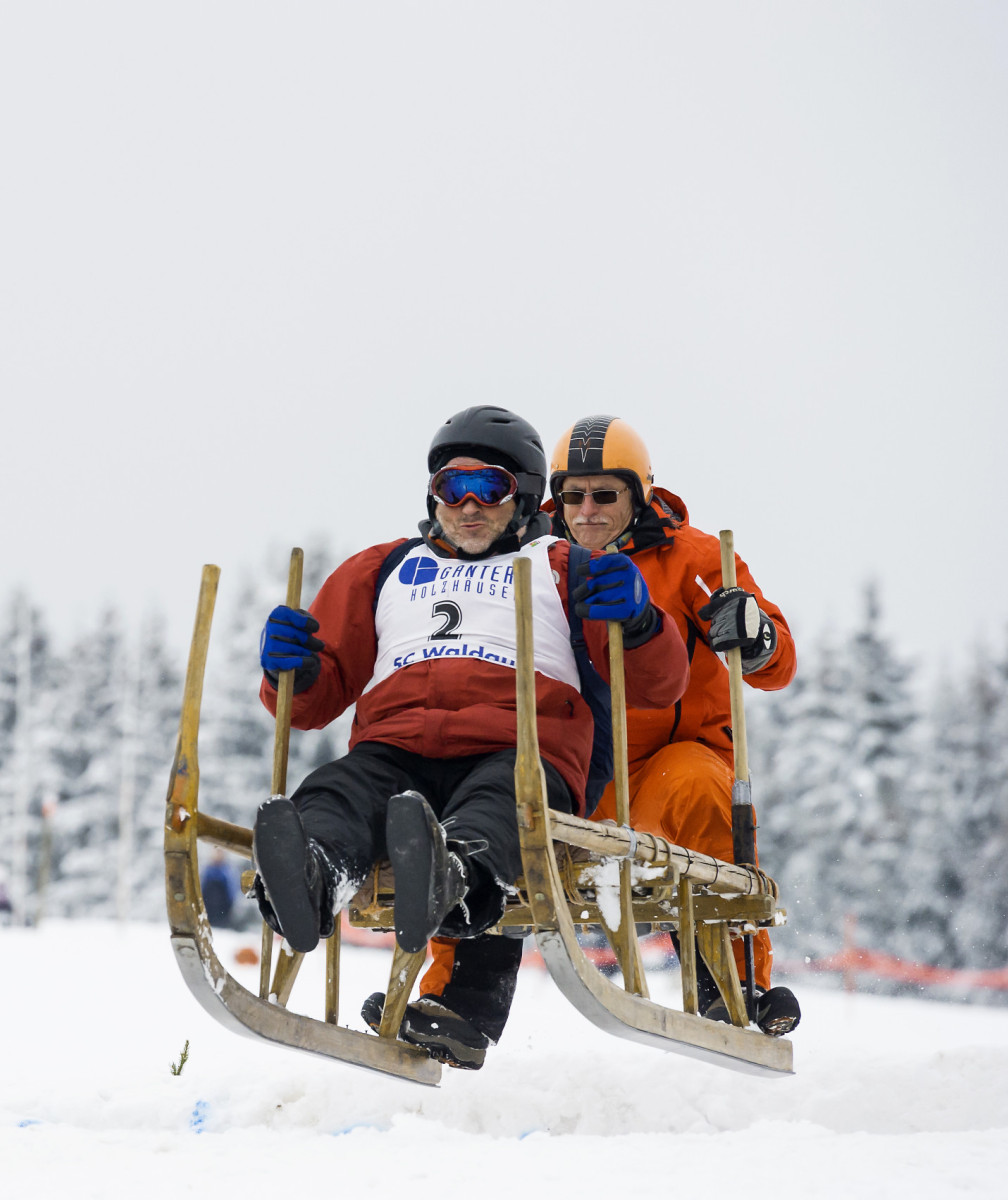 Zwei Personen rasen auf einem Hornschlitten durch den Schnee