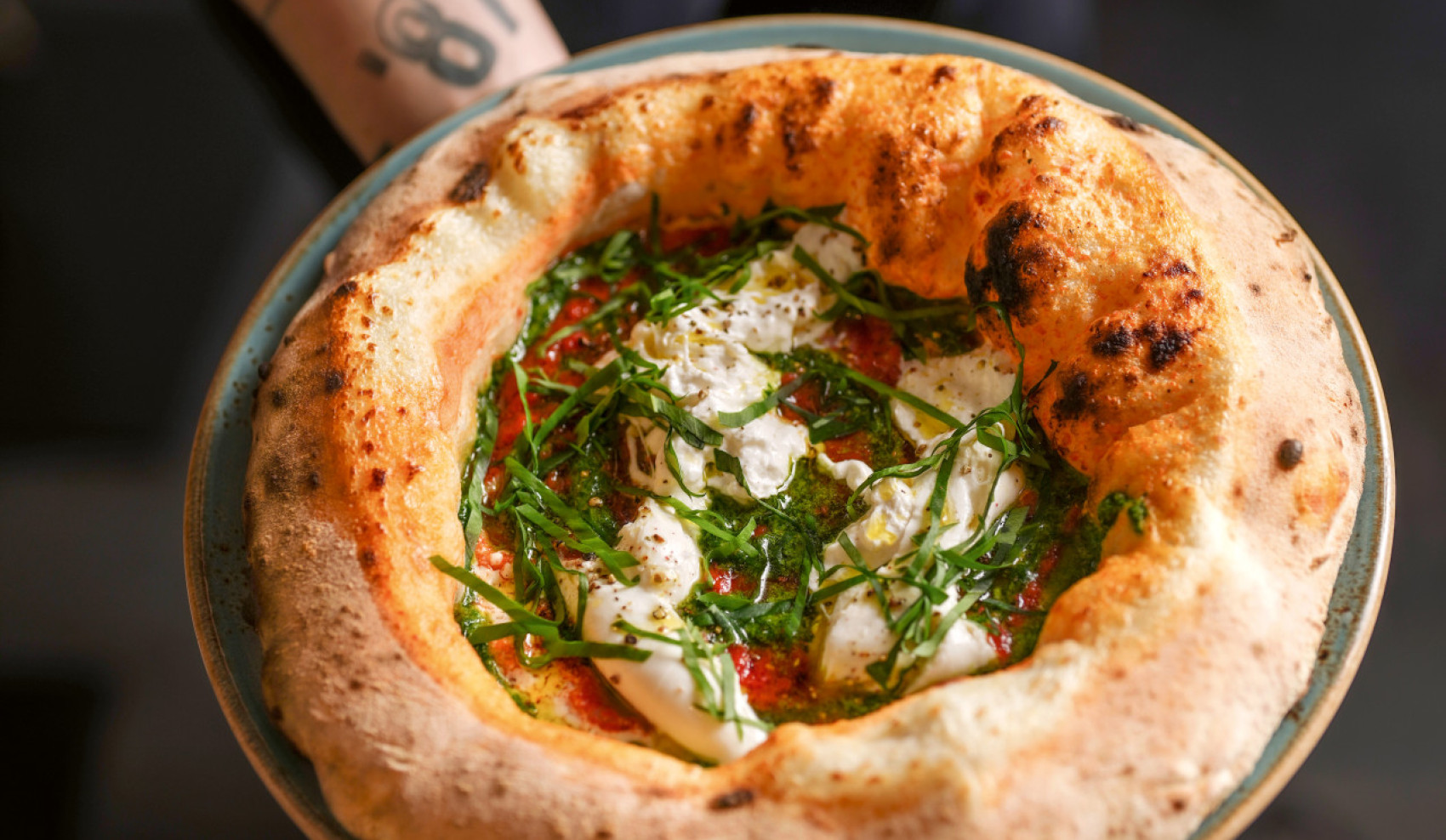Person hält einen Teller mit einer Pizza in die Kamera
