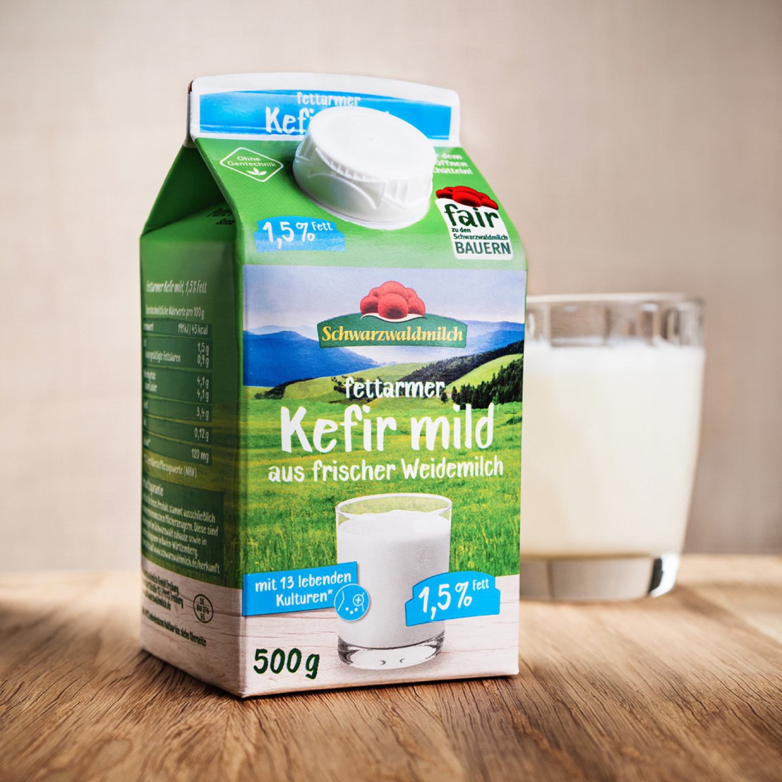 Eine Packung Kefir steht auf einem Tisch, dahinter ein Glas mit Kefir
